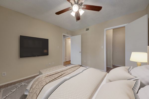 Valley Creek A cozy bedroom with a ceiling fan, TV on the wall, and a neatly made bed with neutral-colored bedding.