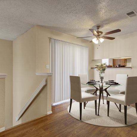 Valley Creek Dining area with a glass table and four white chairs under a ceiling fan, near a kitchen and sliding glass door.