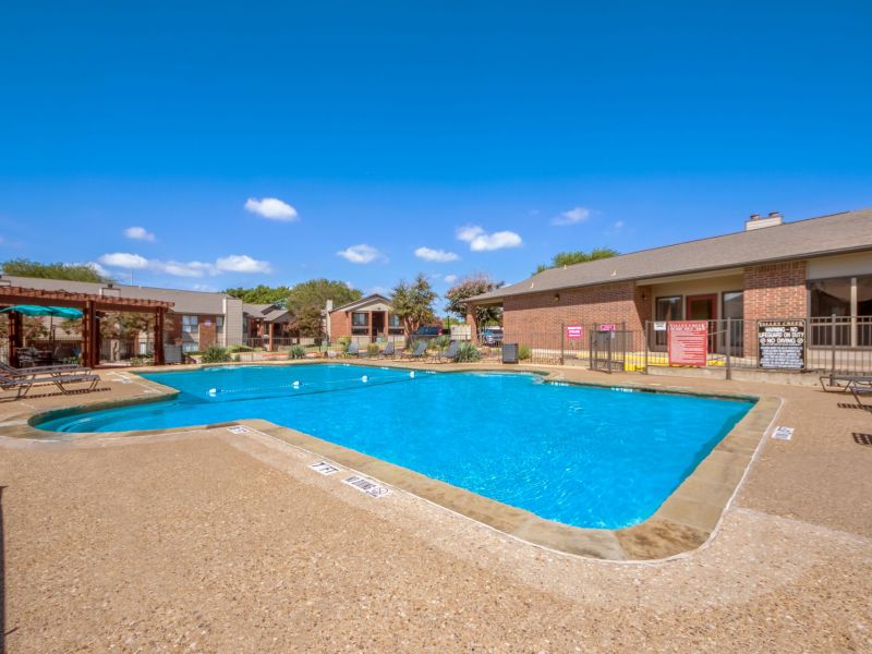 Valley Creek Outdoor swimming pool with clear blue water, surrounded by a concrete deck, lounge chairs, and red brick buildings.