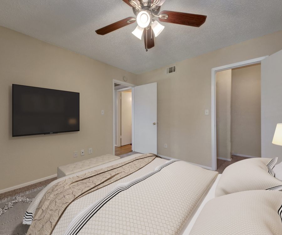 Valley Creek A cozy bedroom with a ceiling fan, TV on the wall, and a neatly made bed with neutral-colored bedding.