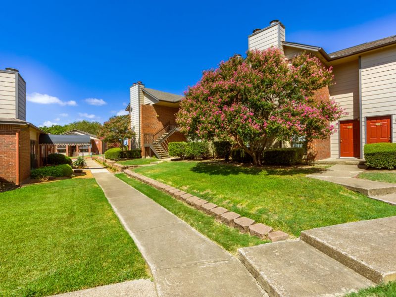 Valley Creek Apartment complex with green lawns, a flowering tree, and red doors under a clear blue sky.