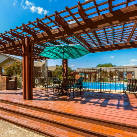 Valley Creek Wooden pergola with seating and an umbrella on a deck near a swimming pool, under a clear blue sky.